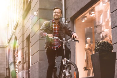 Image of Handsome happy man riding bicycle in city on sunny day, low angle view