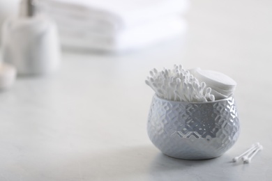 Photo of Cotton buds in holder on white table indoors, space for text