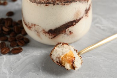 Photo of Tasty tiramisu in glass, coffee beans and spoon on light grey table, closeup