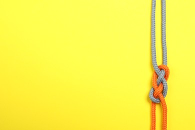 Photo of Top view of colorful ropes tied together on yellow background, space for text. Unity concept