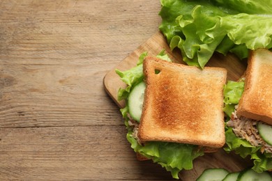 Delicious sandwiches with tuna, cucumber and lettuce leaves on wooden table, flat lay. Space for text