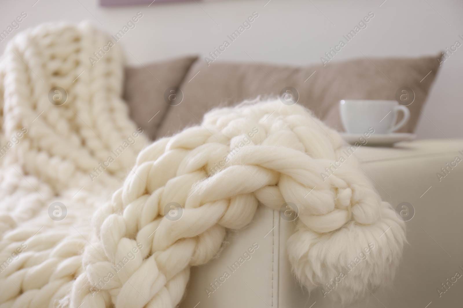 Photo of Soft knitted blanket on couch in room, closeup. Interior element