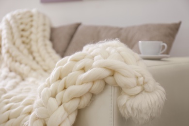 Soft knitted blanket on couch in room, closeup. Interior element