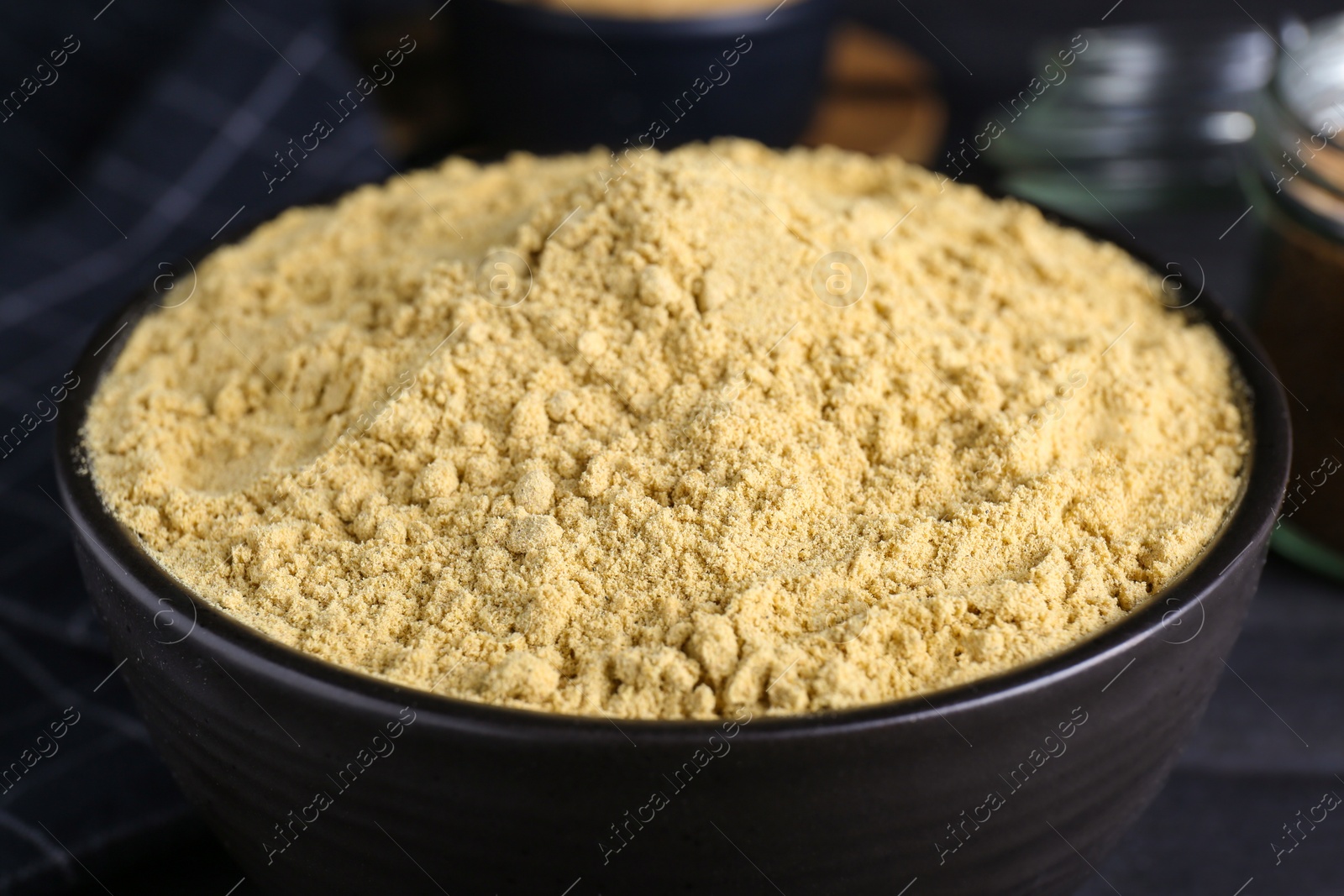 Photo of Bowl of aromatic mustard powder on black wooden table, closeup