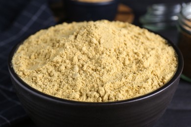 Photo of Bowl of aromatic mustard powder on black wooden table, closeup