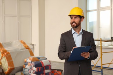 Photo of Professional engineer in hard hat with clipboard indoors