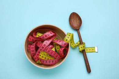 Photo of Measuring tapes and wooden spoon on light blue background, flat lay. Weight loss concept
