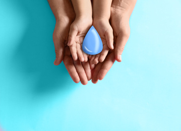 Image of Mother and her child holding water drop on light blue background, top view. Ecology protection