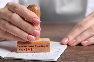 Woman stamping document at wooden table, closeup. Permanent residency visa in Canada