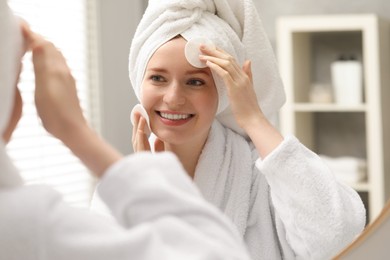 Photo of Smiling woman with freckles wiping face near mirror in bathroom