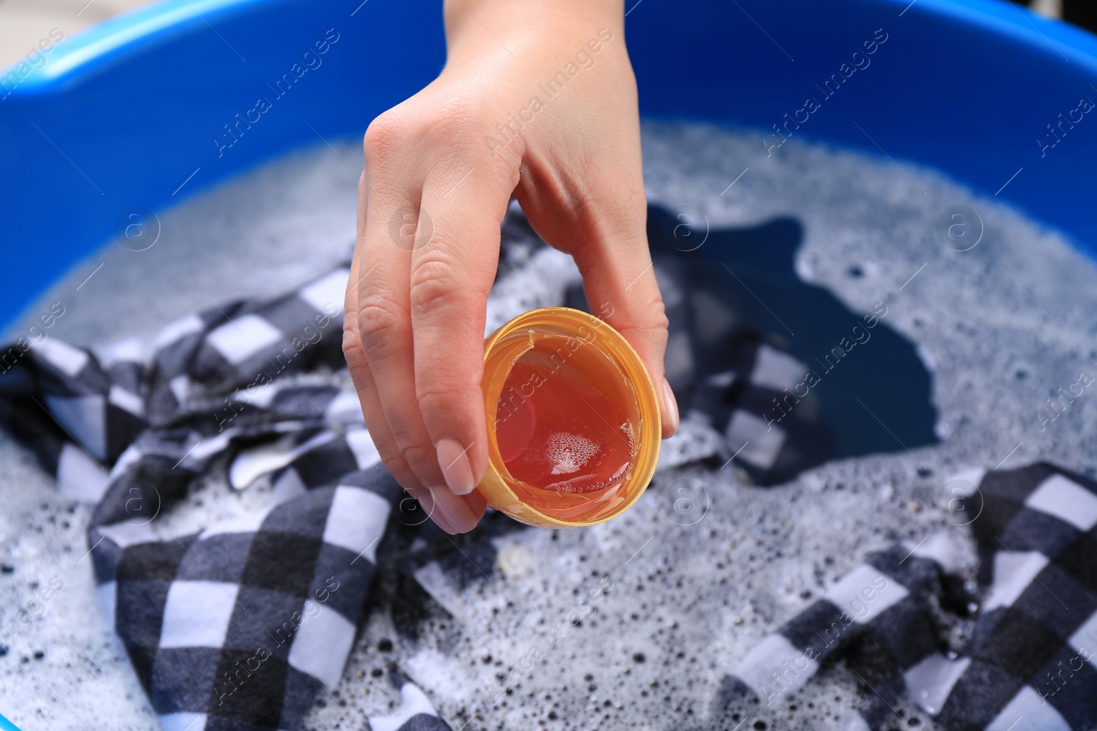 Photo of Woman pouring detergent into basin with clothing, closeup. Hand washing laundry