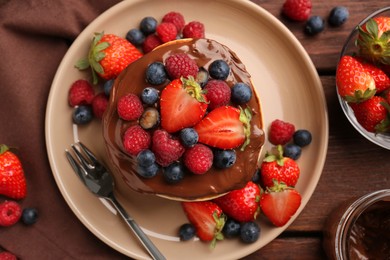 Photo of Stack of tasty pancakes with fresh berries and chocolate spread on wooden table, flat lay