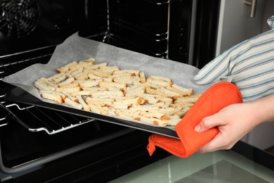 Photo of Woman taking baking pan with hard chucks out of oven, closeup