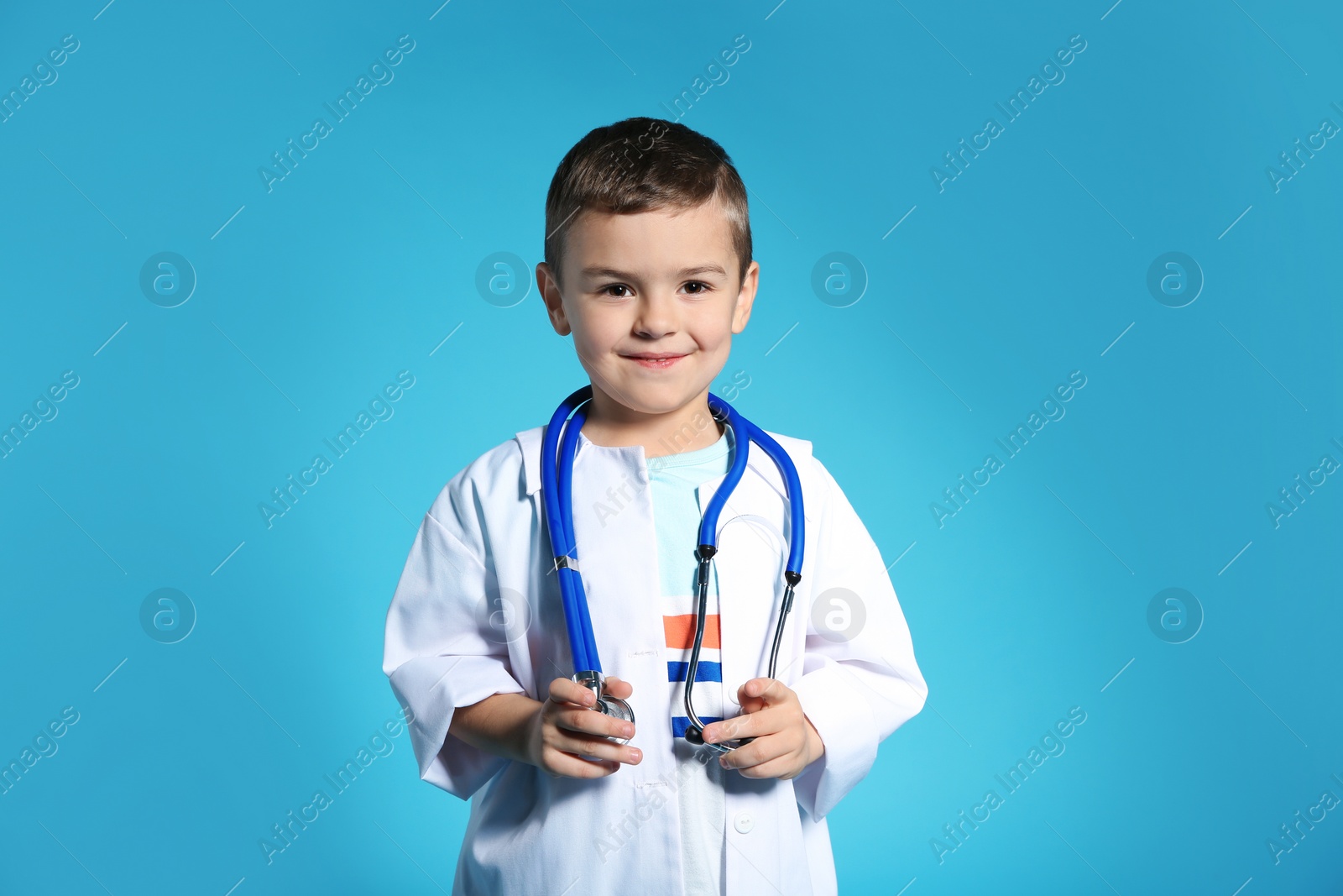 Photo of Cute child in doctor coat with stethoscope on color background