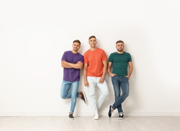 Group of young men in jeans and colorful t-shirts near light wall