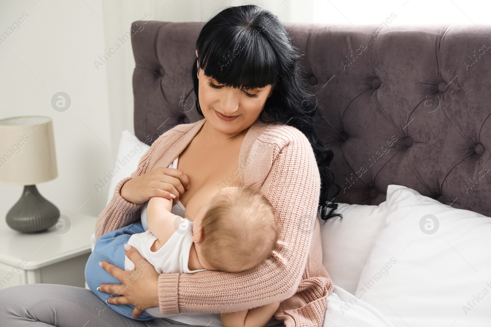 Photo of Woman breastfeeding her little baby on bed indoors