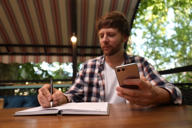 Handsome man using smartphone at table in outdoor cafe, focus on hand