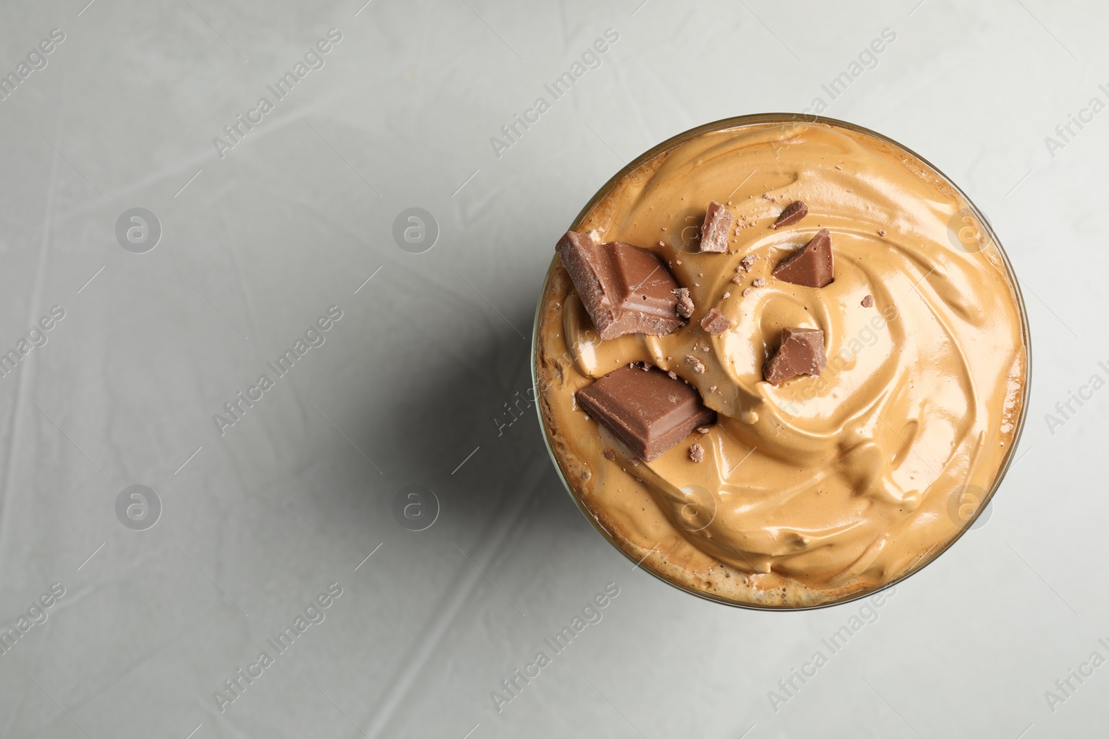 Photo of Glass of delicious dalgona coffee with chocolate on light grey table, top view. Space for text