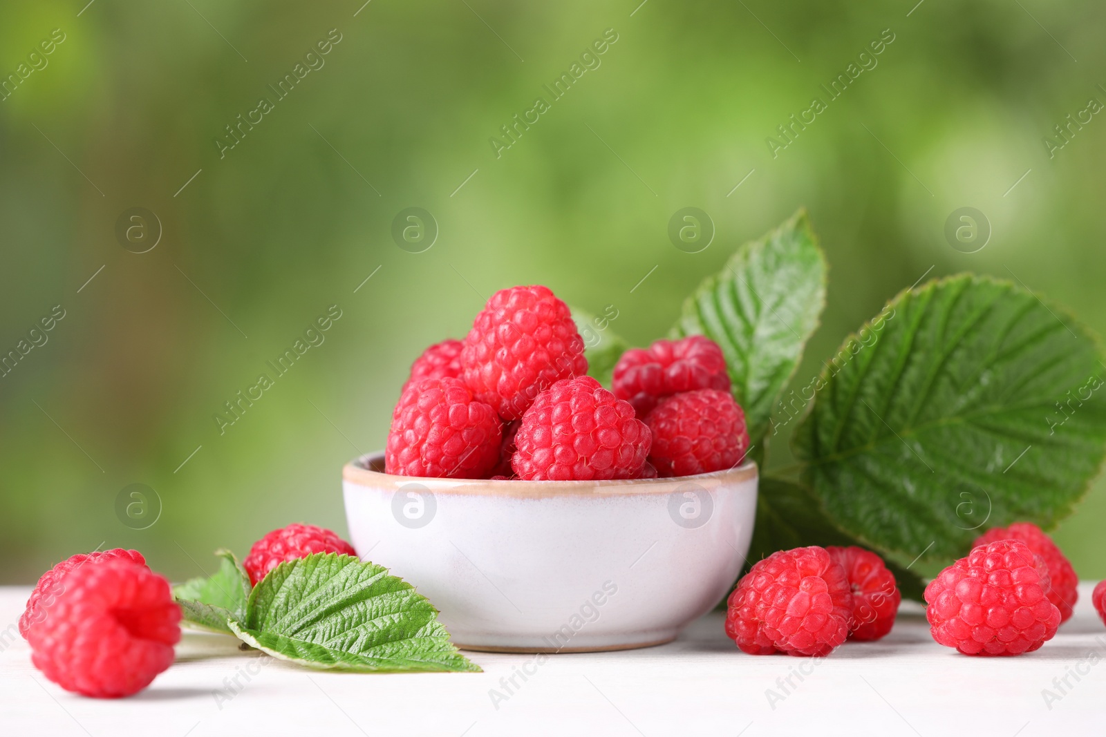 Photo of Tasty ripe raspberries and green leaves on white table outdoors