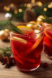 Photo of Delicious punch drink with cranberries and orange on wooden table against blurred festive lights, closeup