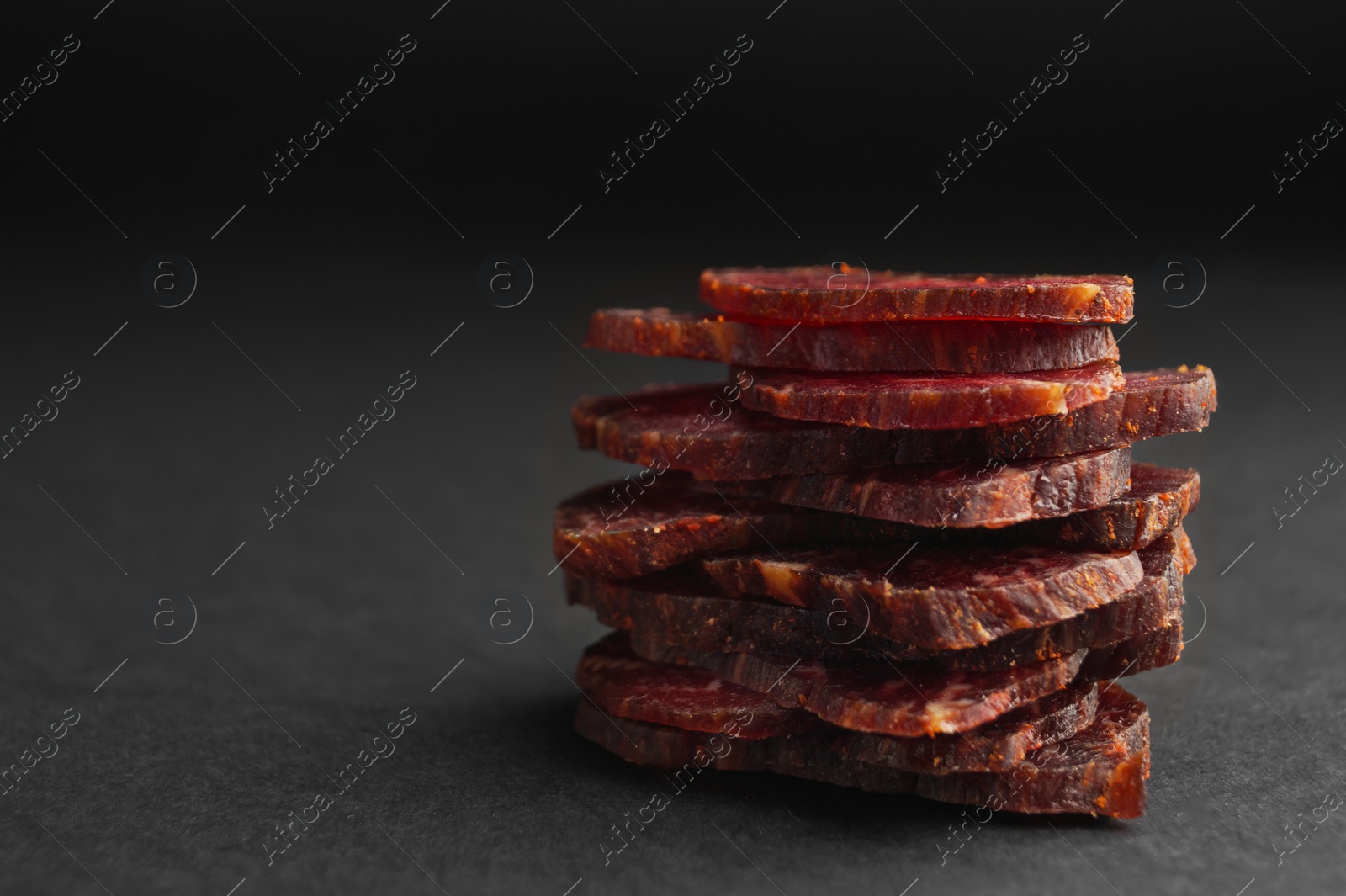 Photo of Stack of delicious beef jerky on dark table, closeup. Space for text