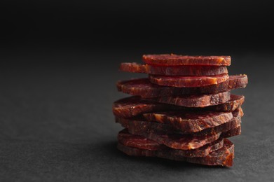 Stack of delicious beef jerky on dark table, closeup. Space for text