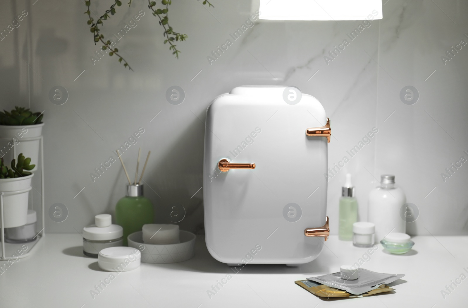 Photo of Cosmetics refrigerator and skin care products on white table indoors