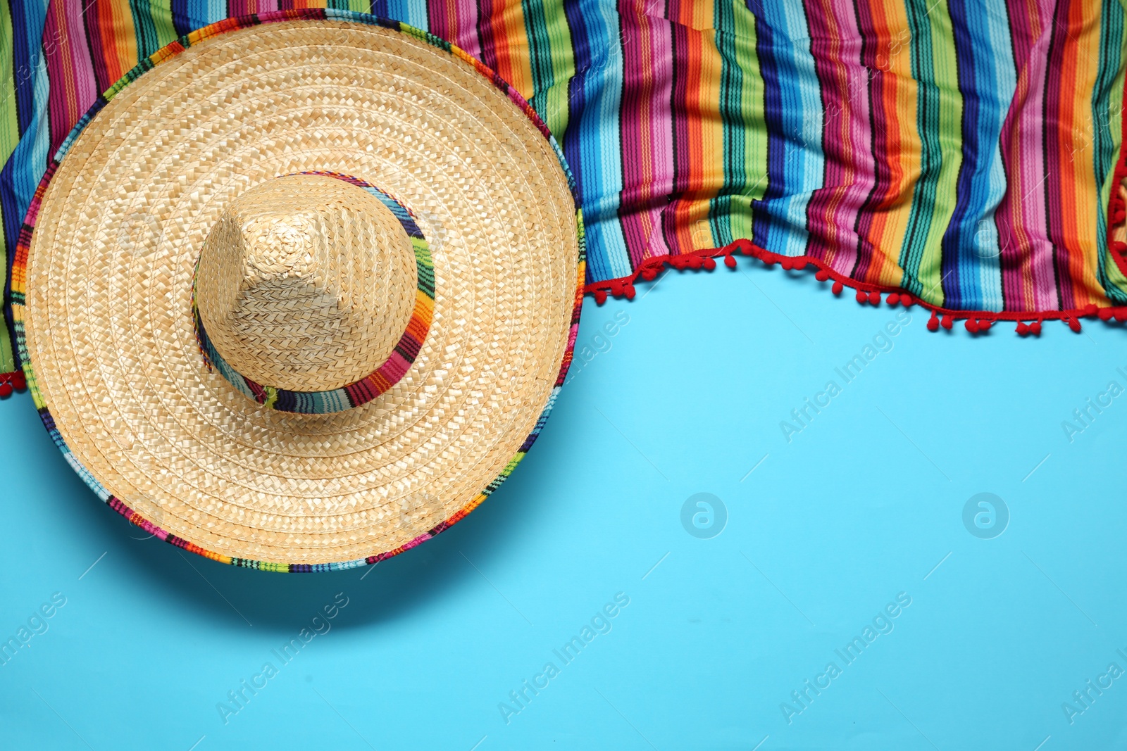 Photo of Mexican sombrero hat and colorful poncho on light blue background, flat lay. Space for text