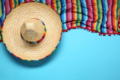 Photo of Mexican sombrero hat and colorful poncho on light blue background, flat lay. Space for text