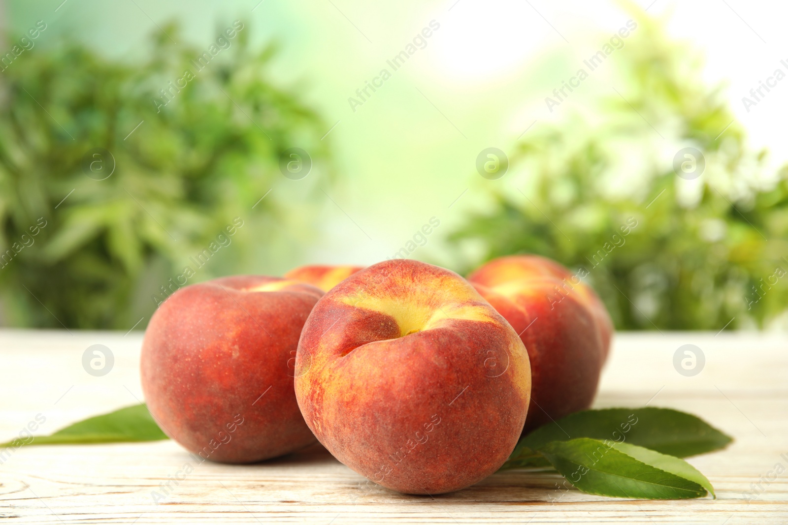 Photo of Fresh peaches and leaves on white wooden table against green blurred background