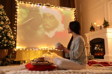 MYKOLAIV, UKRAINE - DECEMBER 24, 2020: Woman watching The Grinch movie via video projector in room. Cozy winter holidays atmosphere
