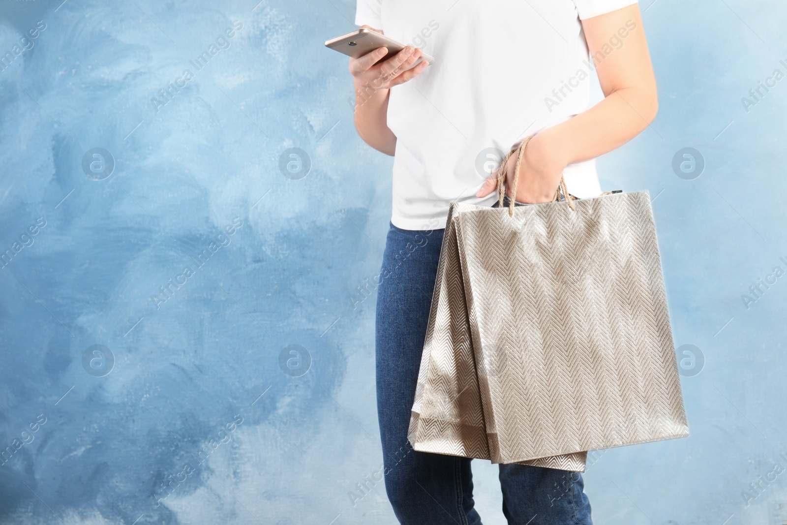 Photo of Woman with silver shopping paper bags and smartphone on light blue background, closeup. Space for text