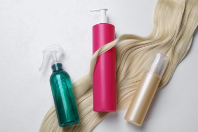 Photo of Spray bottles with thermal protection and lock of blonde hair on white background, flat lay