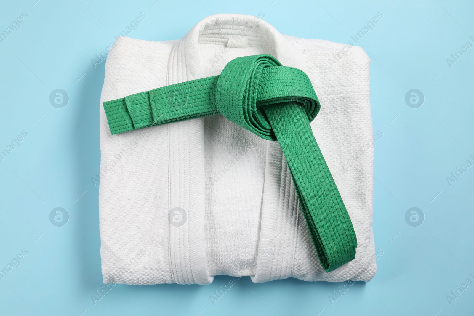 Photo of Green karate belt and white kimono on light blue background, top view