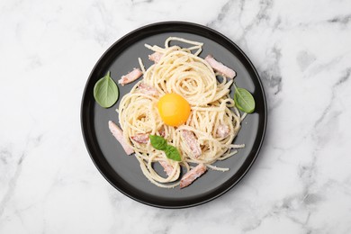 Photo of Plate of tasty pasta Carbonara with basil leaves on white marble table, top view