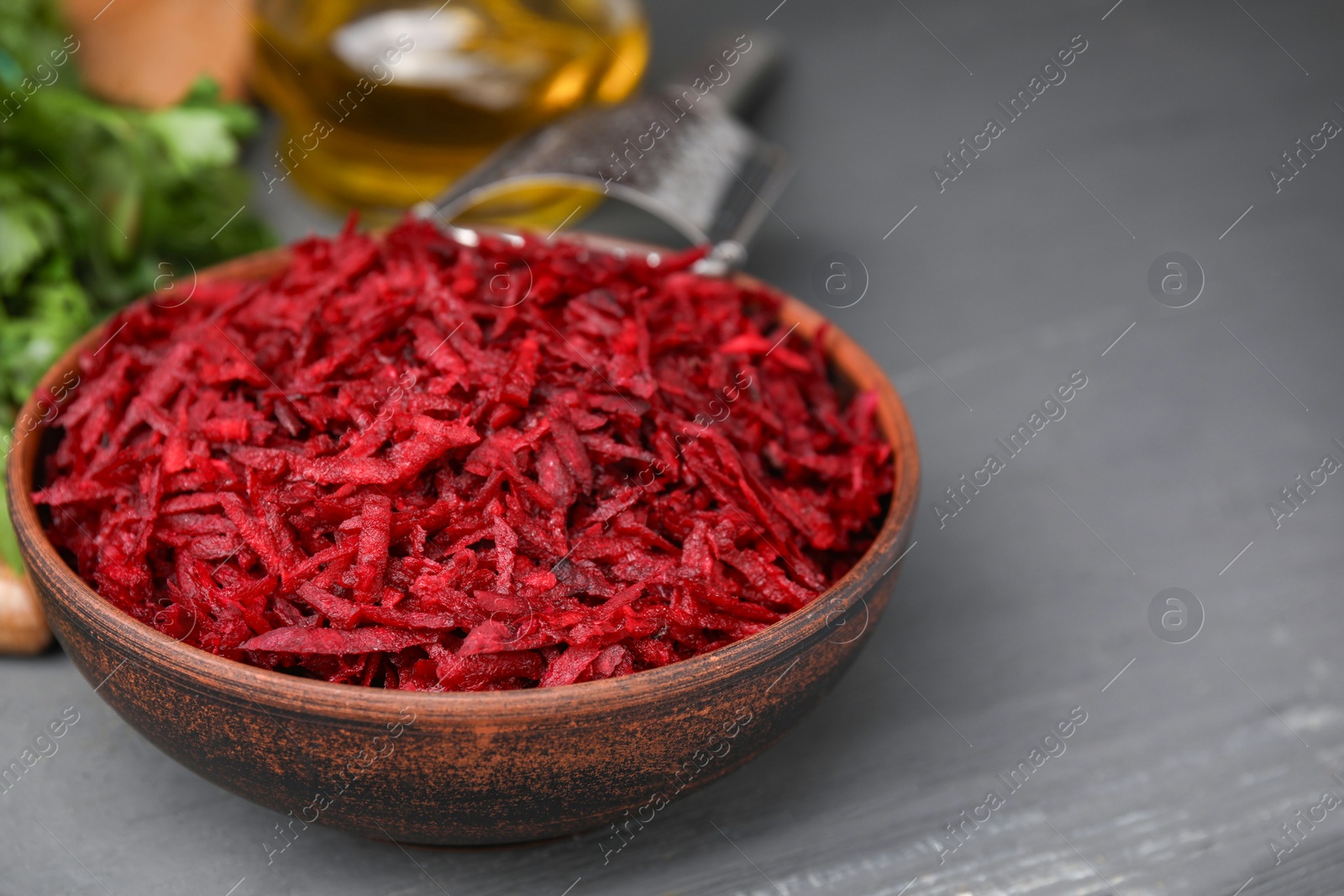 Photo of Grated red beet in bowl on gray table, closeup