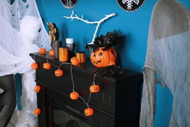 Photo of Jack-o'-lantern lights and different Halloween decorations on black fireplace near blue wall