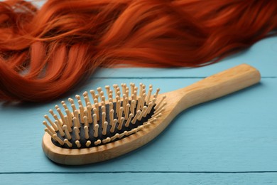 Brush and red hair strand on light blue wooden table