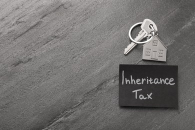 Photo of Inheritance Tax. Card and key with key chain in shape of house on grey table, top view. Space for text