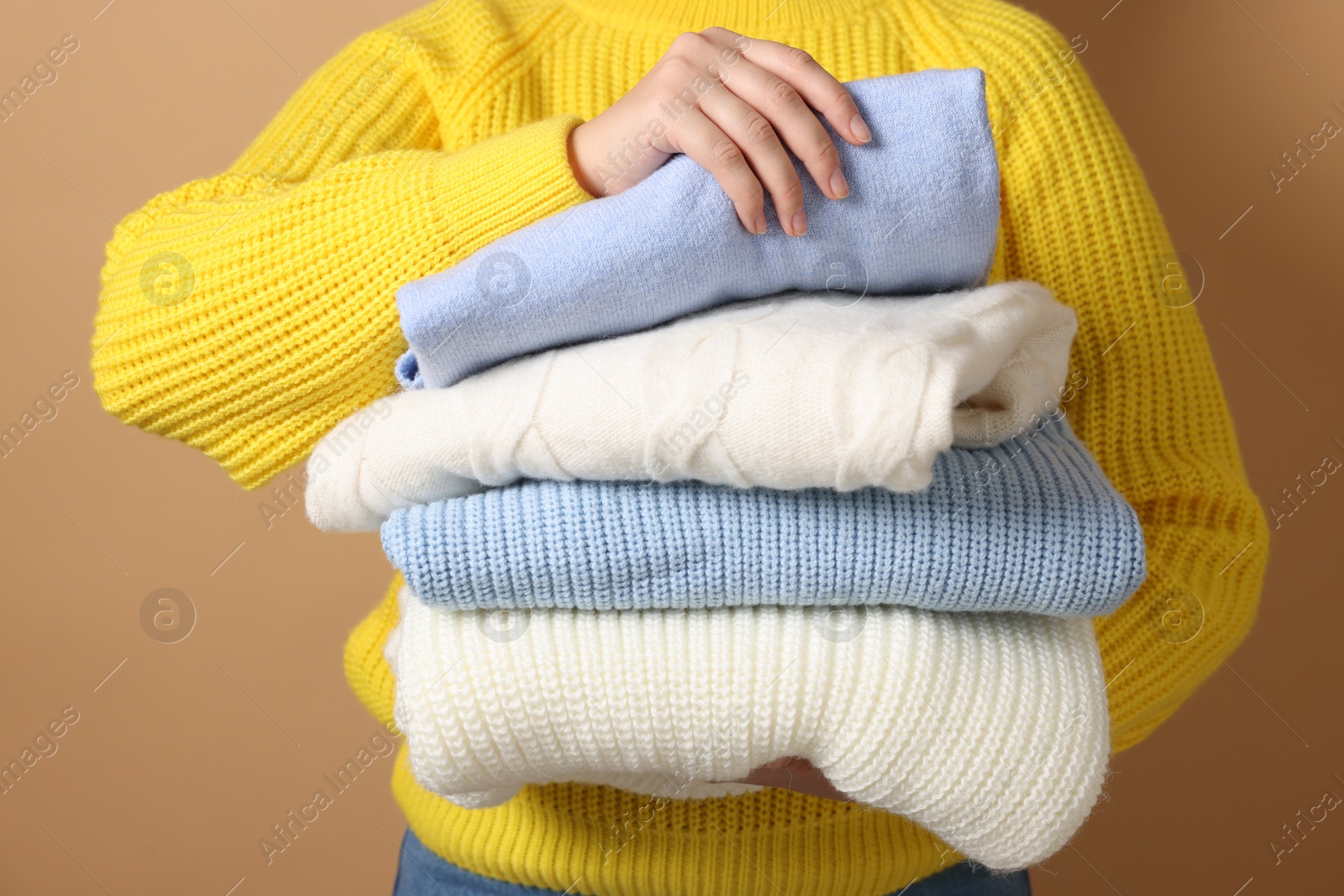 Photo of Woman with stack of casual sweaters on light brown background, closeup