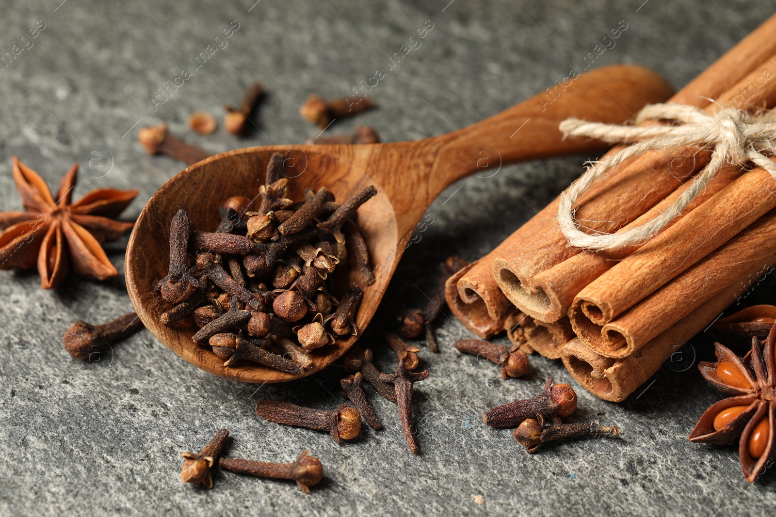 Photo of Wooden spoon with different spices on gray textured table, closeup