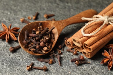 Photo of Wooden spoon with different spices on gray textured table, closeup