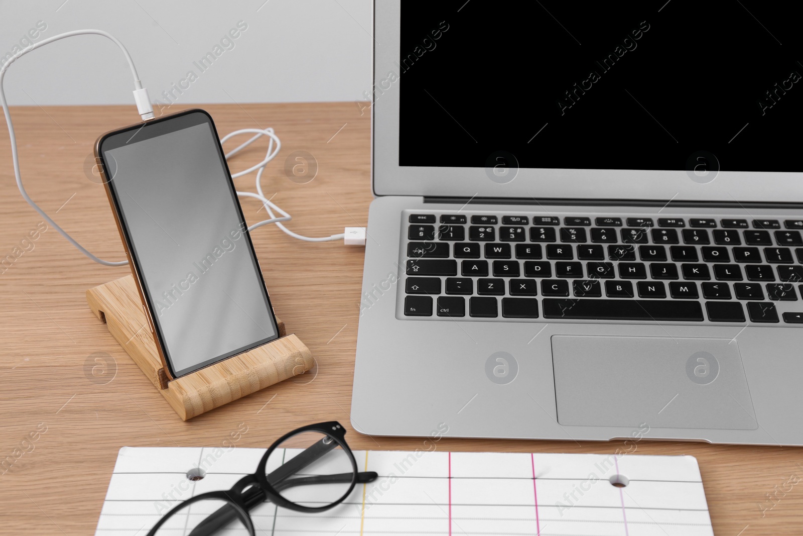 Photo of Modern smartphone charging from laptop on wooden table