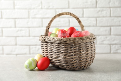 Photo of Wicker basket with colorful painted Easter eggs on table near brick wall