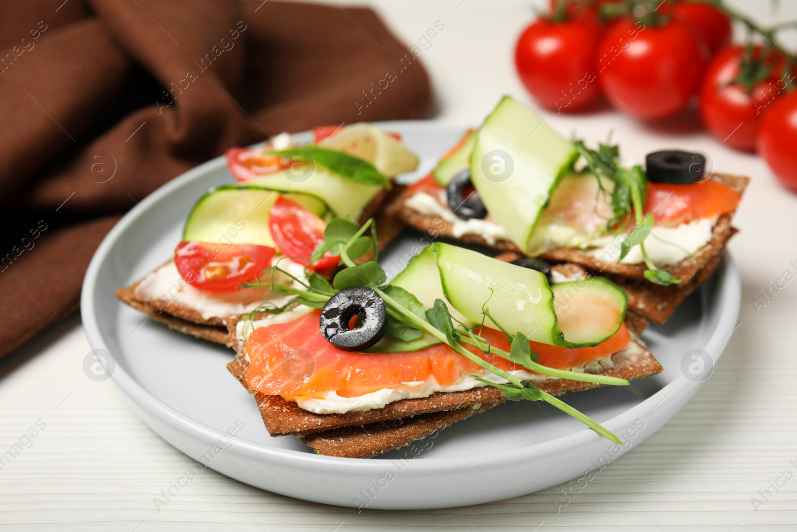 Photo of Tasty rye crispbreads with salmon, cream cheese and vegetables served on white wooden table, closeup