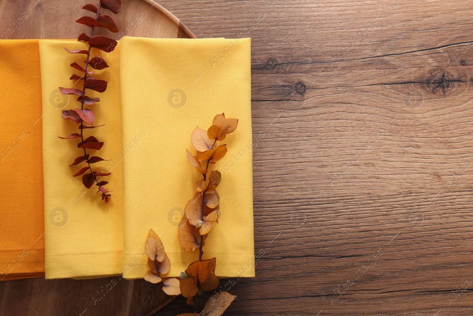 Photo of Tray with different kitchen napkins and decorative dry leaves on wooden table, top view. Space for text