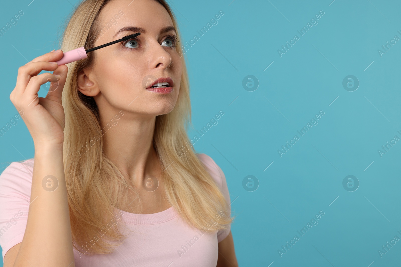 Photo of Beautiful woman applying mascara on light blue background, space for text