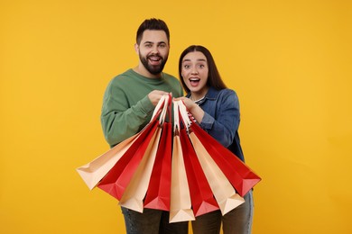 Excited couple with shopping bags on orange background