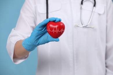 Image of Doctor holding red heart on light blue background, closeup