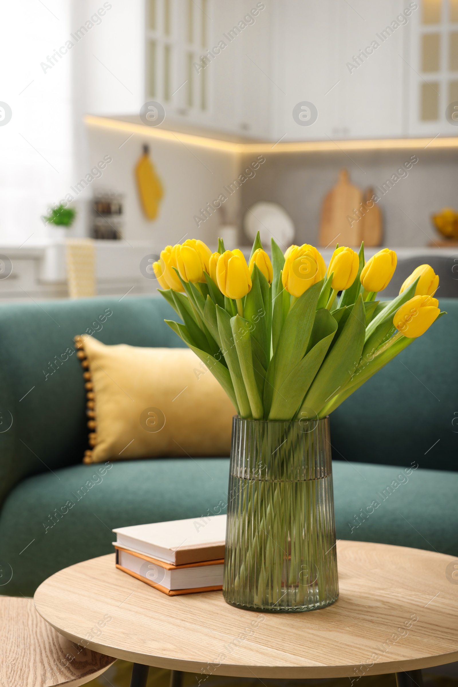 Photo of Spring interior. Bouquet of beautiful yellow tulips and books on wooden table in living room
